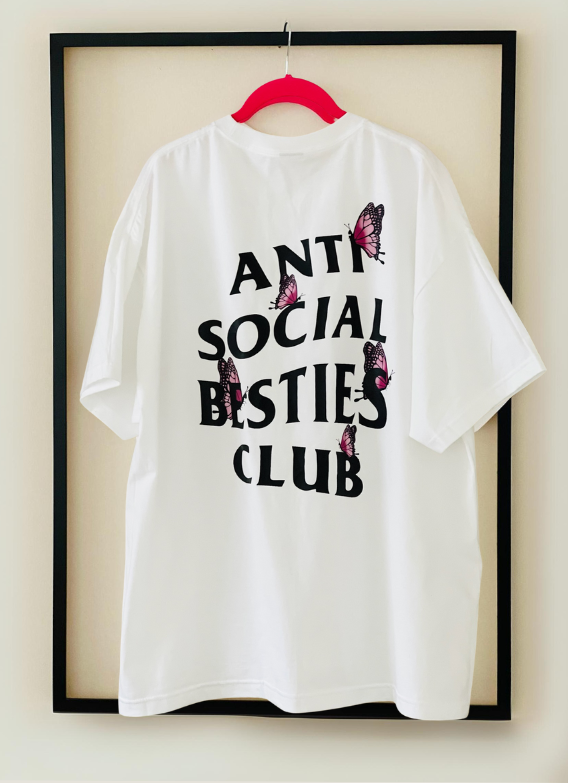 Back view of the white AntiSocial Besties Club Butterfly Tee by Dass My Best Friend, hanging inside a picture frame. The butterfly details and bold design stand out, capturing the playful and edgy style perfect for introverted best friends.