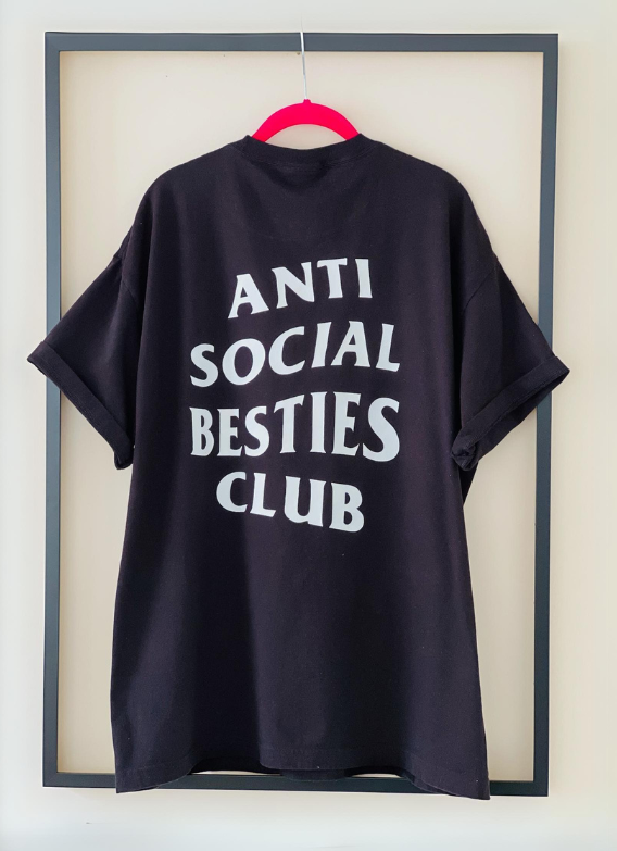 Black AntiSocial Besties Club Tee by Dass My Best Friend. The bold "Antisocial Besties Club" print on her back is clearly visible, showcasing the playful and introverted style designed for best friends.