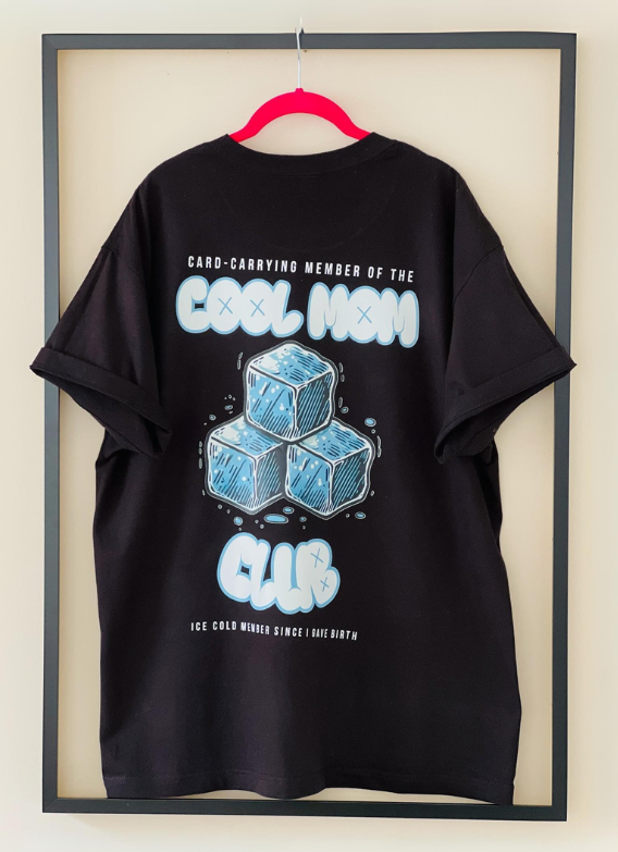 Rear view of the black Cool Mom Club Tee by Dass My Best Friend, hanging inside a picture frame. The bold "COOL MOM CLUB" graphic is displayed on the back, highlighting the relaxed fit and confident style for moms.