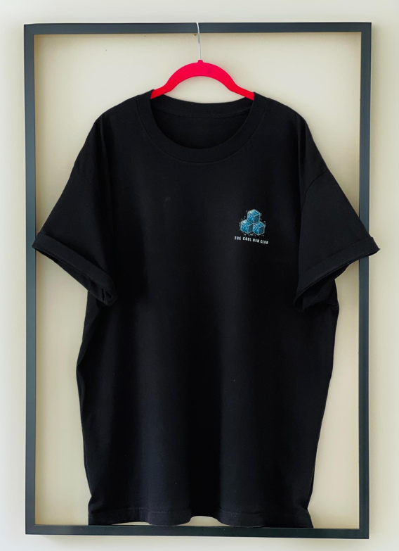 Front view of the black Cool Mom Club Tee by Dass My Best Friend, hanging inside a picture frame. The bold "COOL MOM CLUB" graphic is prominently displayed on the front, showcasing the relaxed fit and stylish design perfect for confident moms.