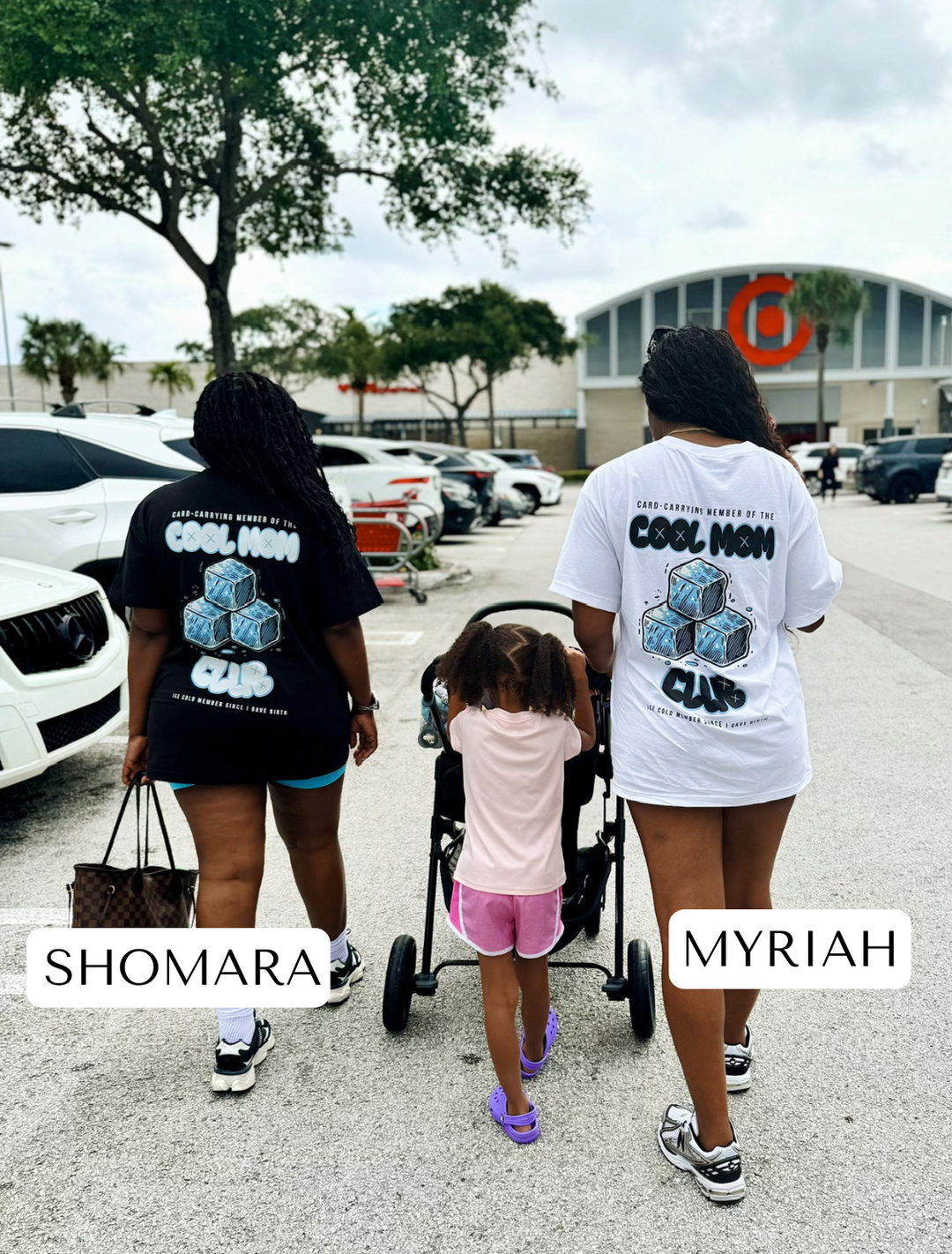 Shomara and Myriah walking through the Walmart parking lot with a child and a baby in a stroller. Myriah is wearing the white Cool Mom Club Tee, and Shomara is in the black version by Dass My Best Friend. The relaxed-fit tees feature the bold "COOL MOM CLUB" graphic, perfect for confident and laid-back moms on the go.