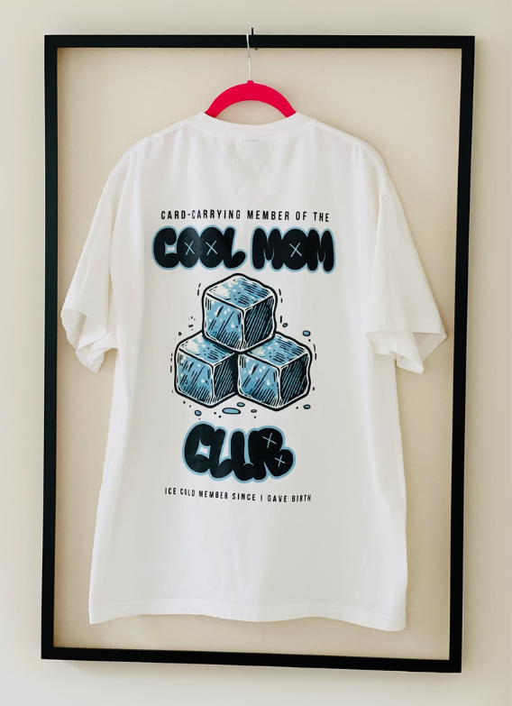 Full back view of the white Cool Mom Club Tee by Dass My Best Friend, hanging inside a picture frame. The bold "COOL MOM CLUB" graphic is showcased on the back, emphasizing the relaxed fit and stylish design for confident moms.