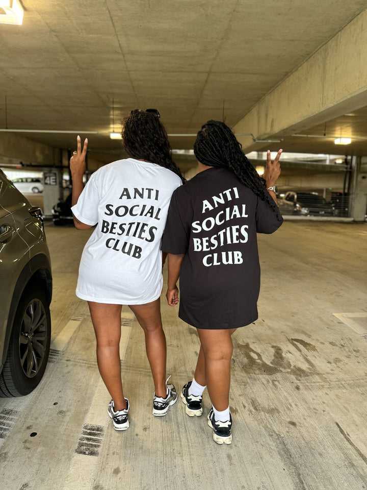 Full back view of two besties wearing Dass My Best Friend 'AntiSocial Besties Club' t-shirts, one in white and the other in black, with large black and white text on the back reading 'ANTISOCIAL BESTIES CLUB'