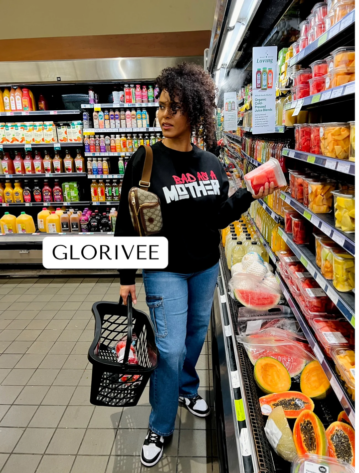 Glorivee standing further away while buying fruit at Whole Foods, wearing a Dass My Best Friend Bad As A Mother graphic sweatshirt in black and gray. The cozy midweight cotton blend sweater offers a stylish and casual fit, perfect for everyday activities like grocery shopping.