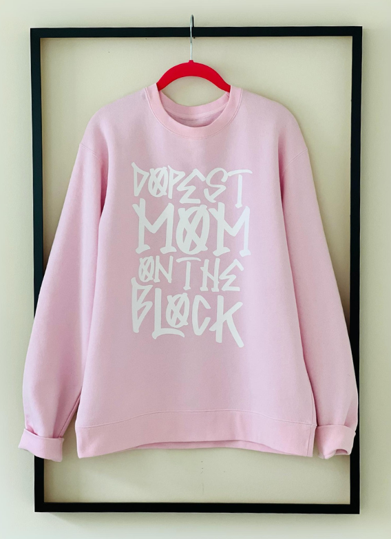 "Dopest Mom on the Block" sweatshirt by Dass My Best Friend, hanging inside a picture frame. The bold design showcases the ultimate confidence for moms, offering a cozy and stylish oversized fit, perfect for any casual occasion.