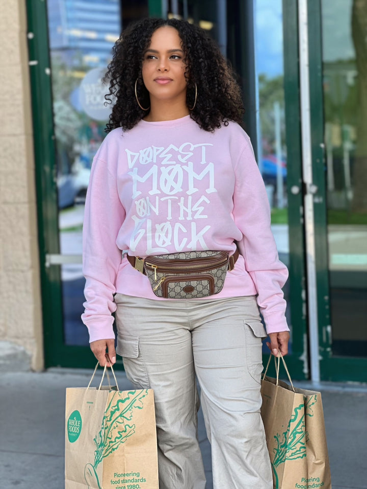 Mom wearing the pink "Dopest Mom on the Block" sweatshirt by Dass My Best Friend, seen from a distance while shopping with a Gucci pouch and carrying two grocery bags from Whole Foods. The bold sweatshirt exudes confidence and style, perfect for busy, fashionable moms.