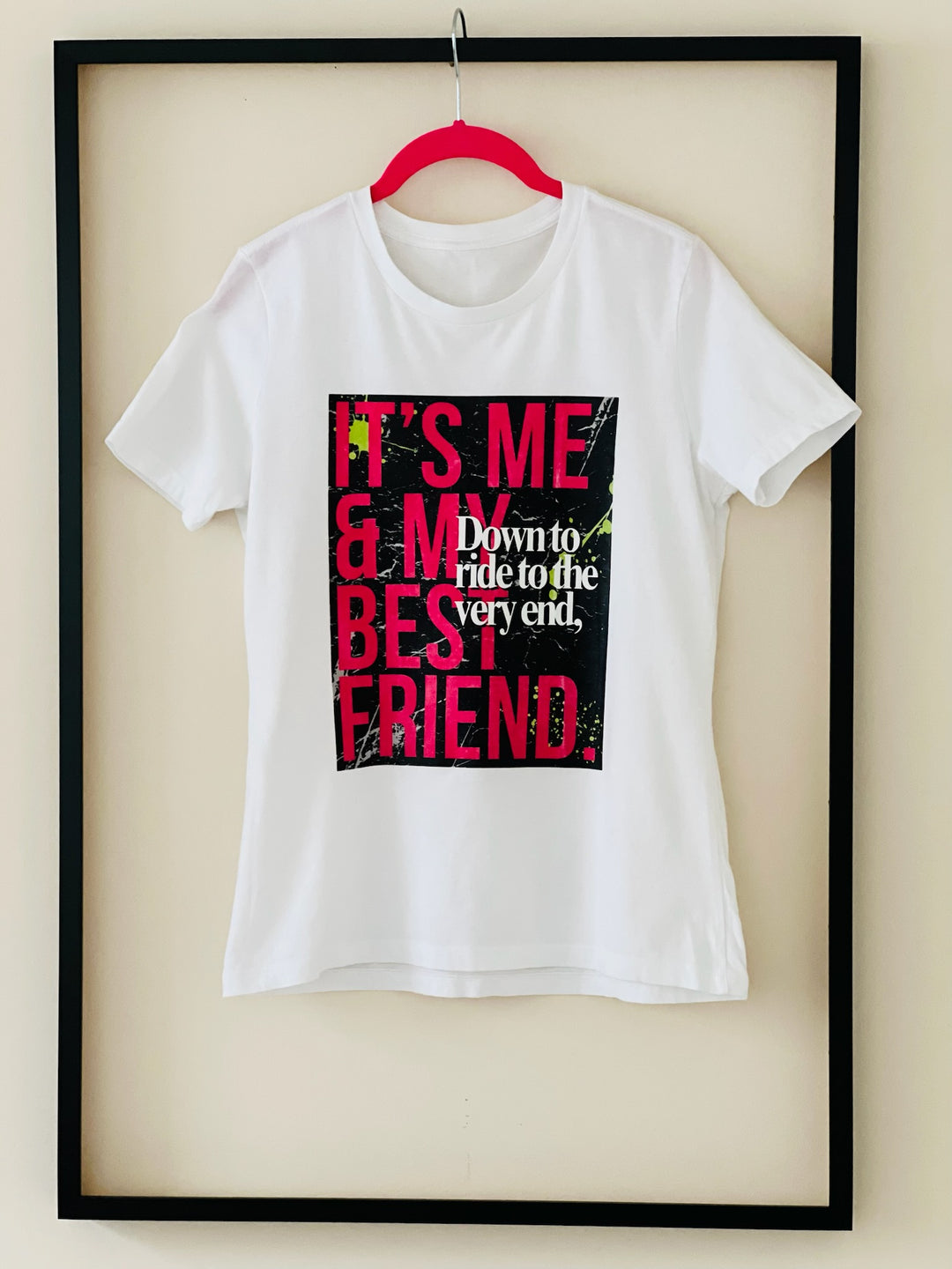 Back view of the "Down to Ride" T-shirt by Dass My Best Friend, hanging inside a picture frame. The feminine-fitted tee showcases its sleek design from behind, celebrating the adventurous spirit of best friends.