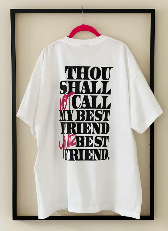 Rear view of the white "Thou Shall Not" Tee by Dass My Best Friend, hanging inside a picture frame. The bold "Thou Shall Not" graphic is displayed on the back, showcasing the oversized fit and playful message.